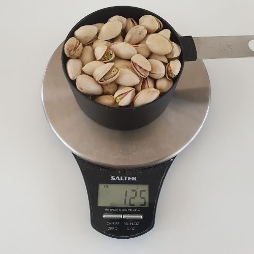 image to show a US cup of unshelled pistachios on a scale weighing 125g
