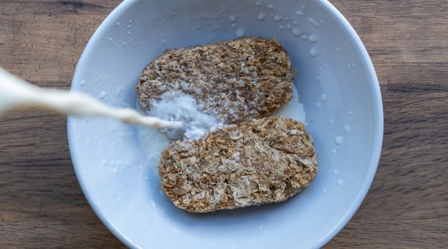 two Weetabix in a bowl with milk being poured over