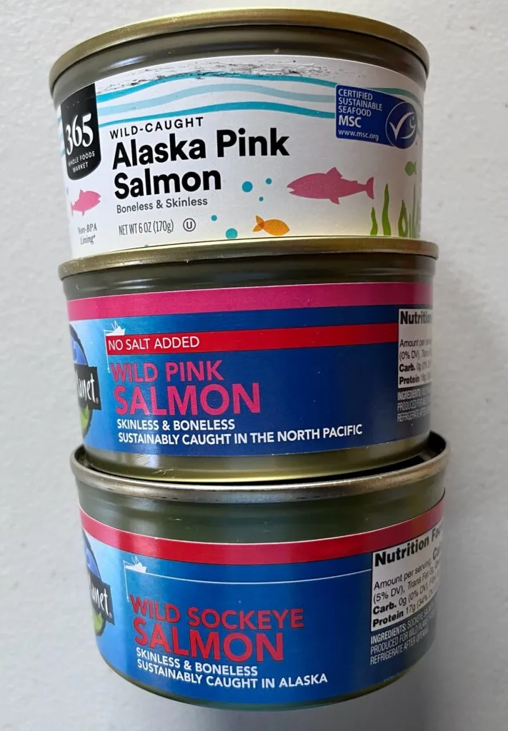 Showing a photo of 3 canned salmon. 2 pink wild salmon cans and one wild sockeye salmon.
