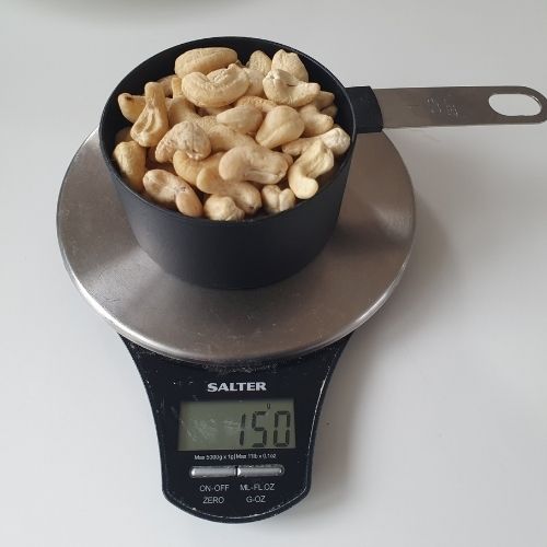 image to show c US cup of cashews on a scale weighing 150g